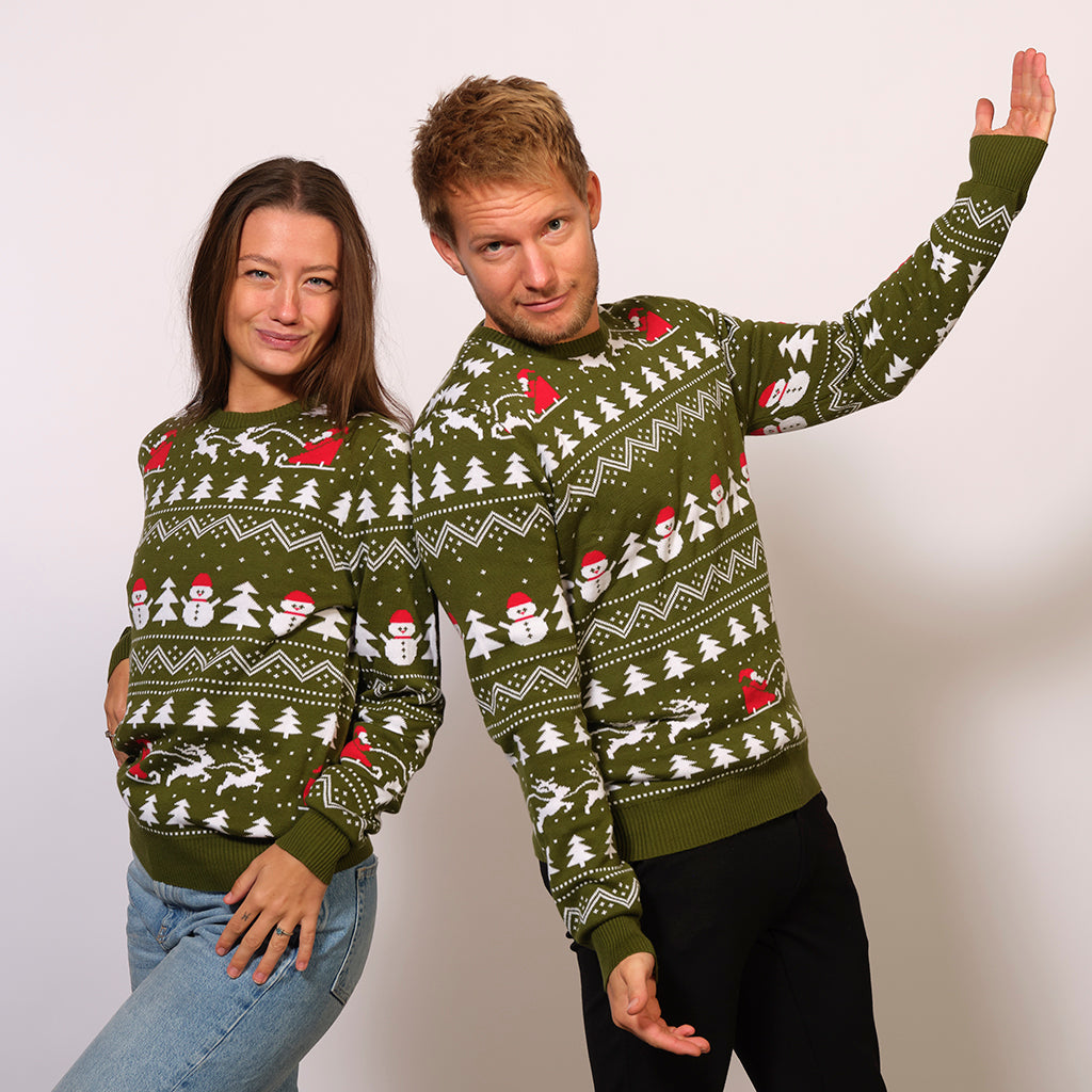 Un couple posant avec un pull de Noël vert avec des arbres de Noël, des pères Noël et des motifs de Noël.